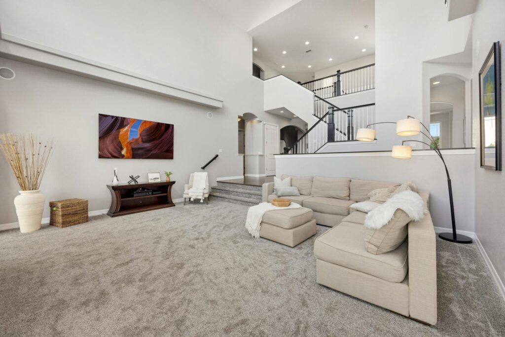 Spacious modern living room featuring a beige sectional sofa, large flat-screen TV, and elegant staircase.