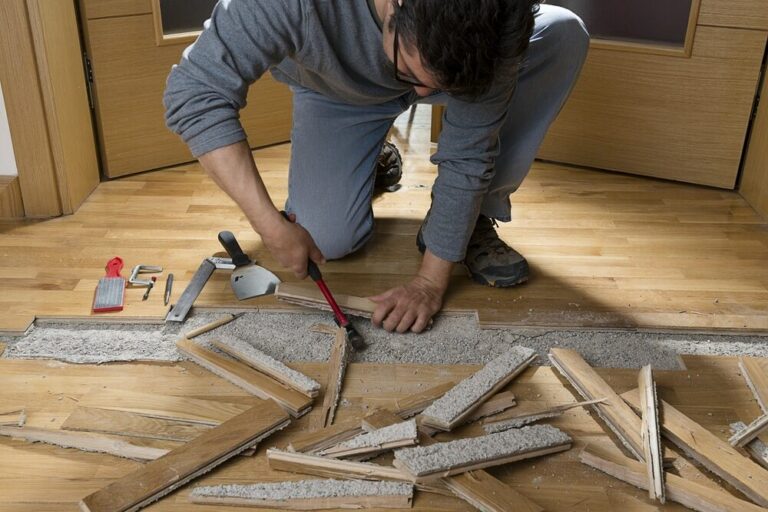 Man repairing floor with tools, surrounded by broken flooring materials.